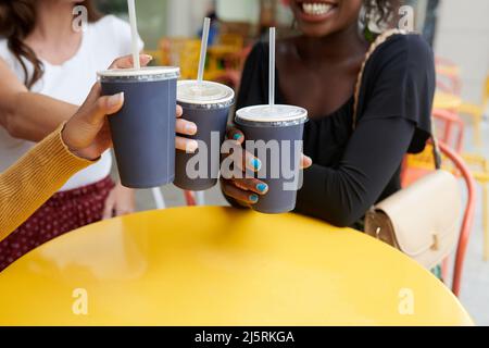 Nahaufnahme von Freundinnen, die Plastikgläser mit alkoholfreien Getränken über dem Kaffeetisch klimpten Stockfoto