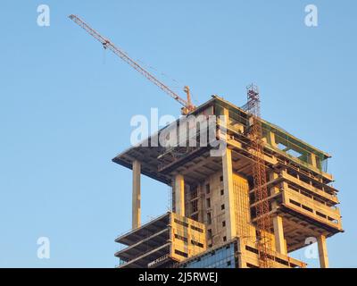 Vergrößerte Aufnahme eines im Bau befindlichen Gebäudes mit grünen Sicherheitsnetzen und einem Kran auf dem halbfertigen Hochhaus, das ein mehrstöckiges Gebäude zeigt Stockfoto