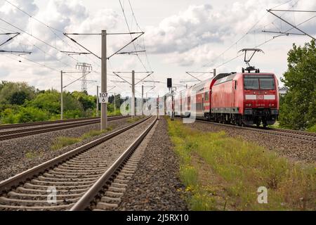 Roter Zug der Deutschen Bahn, der auf der Eisenbahn in ein kleines Dorf rollt. Öffentliche Verkehrsmittel verbinden Dörfer in einer ländlichen Gegend. Elektrisch Stockfoto