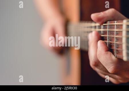 Nahaufnahme des nicht erkennbaren kaukasischen Mannes, der akustische Gitarre spielt, Fokus auf die linke Hand, Kopierraum, Musik- und Unterhaltungskonzept. Stockfoto