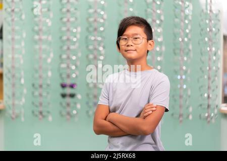 Ein asiatischer Junge, der in einem Optikerladen an einer Brille versucht. Stockfoto