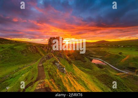 Sonnenuntergang mit Sonnenstern in Schottland auf der Isle of Skye. Landschaft mit Felsen Schloss Ewen im Sommer. Gelb orange roten Himmel mit Wolken. Sandstraße Stockfoto