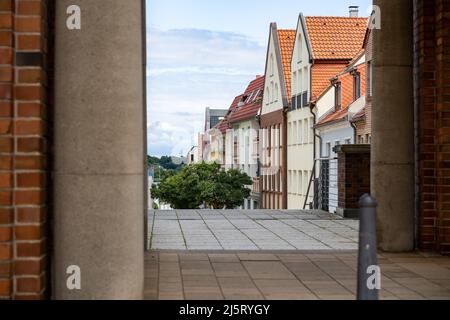 Blick durch einen Durchgang zu einer Reihe von Gebäuden. Häuserfassaden neben den Docks in Rostock. Säulen und Wände aus roten Ziegeln als Rahmen. Stockfoto