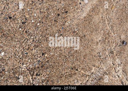Wasser aus dem Meer bewegt sich über den Sand eines Strandes. Blick von oben auf eine idyllische Urlaubsszene. Natürlicher Kiesboden auf dem Boden. Stockfoto