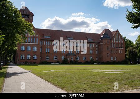 Hansa-Gymnasium in der Stadt. Bau der Sekundarschule in einer alten Architektur. Das Haus ist aus roten Ziegeln gebaut. Ein Platz mit Gras davor. Stockfoto