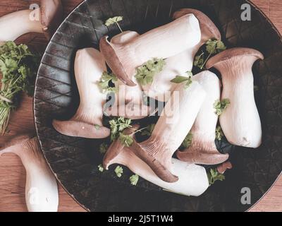 Rohe Königsausternpilze auf einer eisernen Pfanne, die mit einem wenig - Draufsicht - verziert ist; auf einem hölzernen Küchentafel Stockfoto