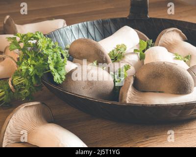 König Austernpilz mit par in eiserner Pfanne auch als eryngii oder König Trompete Pilz auf einem hölzernen Schneidebrett bekannt Stockfoto