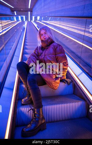 Junges Mädchen, das auf den Rolltreppen der U-Bahn sitzt, junger kaukasischer Teenager im Winter Stockfoto