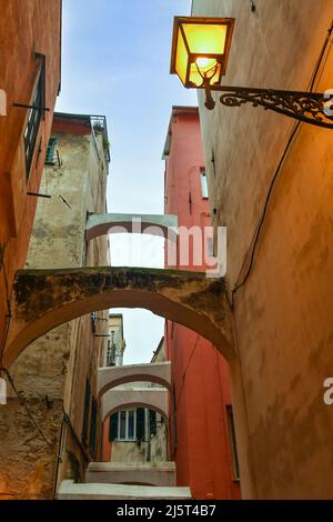 Blick auf eine schmale Gasse ('caruggio') im historischen Zentrum von Sanremo, mit den typischen pastellfarbenen Häusern in der Abenddämmerung, Imperia, Ligurien Stockfoto