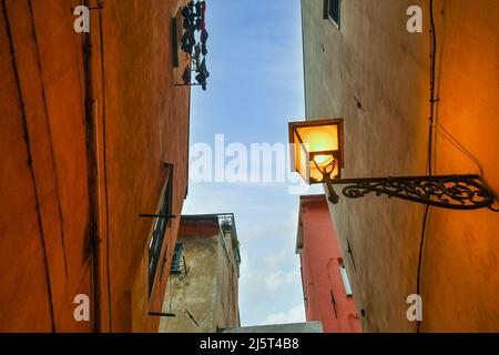 Blick auf eine beleuchtete Straßenlampe in einer engen Gasse des historischen Zentrums von Sanremo in der Abenddämmerung, Imperia, Ligurien, Italien Stockfoto