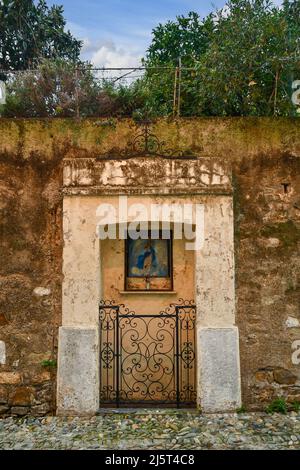 Detail einer alten Steinmauer mit einem Votivschrein, der von einem schmiedeeisernen Tor in einer gepflasterten Gasse der Altstadt von Sanremo, Imperia, Ligurien geschlossen wurde Stockfoto