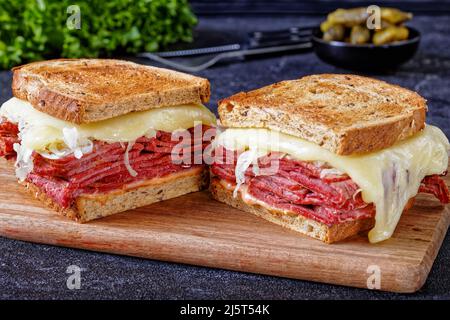 reuben-Sandwich mit Roggenbrot in dünne Scheiben geschnittenes Corned Beef, Sauerkraut, Tausendinseln-Sauce und geschmolzenem Käse an Bord mit Gurken und frischem Salat Stockfoto