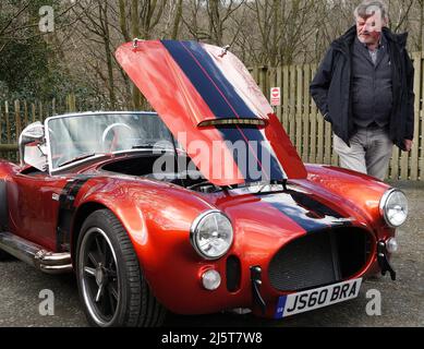 Ein kraftvoll aussehendes rotes AC Cobra-Auto bei der Oldtimer-Show mit einem Bewunderer, der sich anschaut Stockfoto