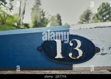 Eine alte Metallplatte, die auf einem Holzbalken befestigt ist und auf der die Ziffern 13 eingeprägt sind Stockfoto