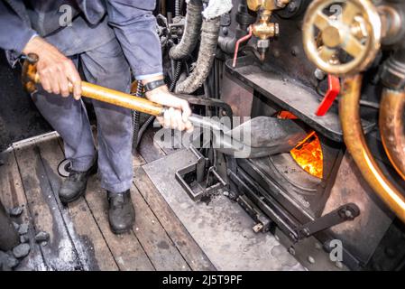 Kohle wird in die Feuerstelle einer Dampflokomotive geschaufelt. Ingenieur, Fahrer, Feuerwehrmann in der Kabine von Hunslet Sparity 0-6-0 Fütterung Kohle Brennkessel Stockfoto