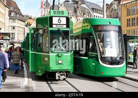 Basel, Schweiz - April 2022: Moderne elektrische Straßenbahn und eine alte Straßenbahn nebeneinander. Die Stadt verfügt über ein ausgedehntes Straßenbahnnetz Stockfoto