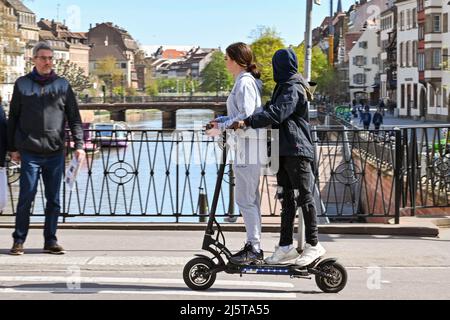 Straßburg, Frankreich - 2022. April: Zwei Personen fahren mit einem Elektroroller über eine Kanalbrücke in Straßburg. Stockfoto