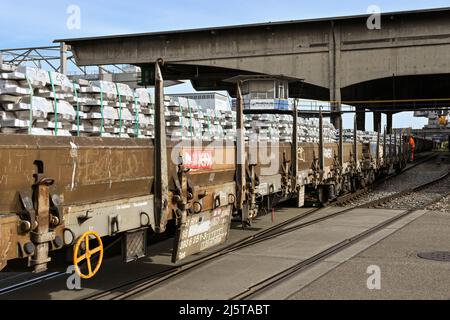 Basel, Schweiz - April 2022: Zug mit Metallbarren überquert eine Straße im Hafen der Stadt am Rhein Stockfoto