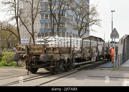 Basel, Schweiz - April 2022: Eisenbahner beobachtet das Ende eines Zuges mit Metallbarren, der eine Straße im Hafen am Rhein überquert Stockfoto