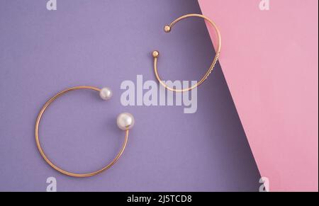 Zwei moderne goldene Armbänder auf rosa und violettem Hintergrund mit Kopierfläche Stockfoto