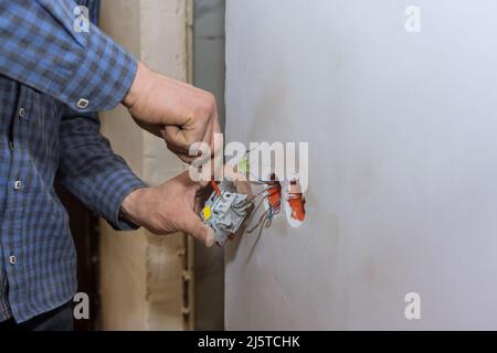 Hände eines Elektrikers, der einen Schraubendreher hält, der an der Hausstromversorgung arbeitet und eine Steckdose an der Wand installiert Stockfoto