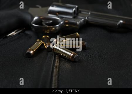 .44 Magnum Revolver und Munitionsmittel auf einer schwarzen Biker-Jacke mit Lederhintergrund Stockfoto