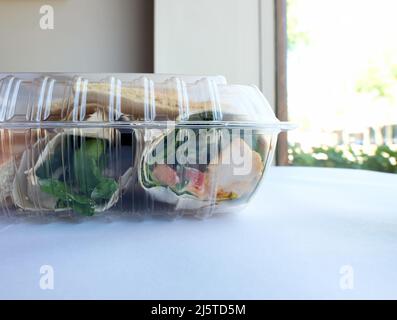 Klare Plastikreste-Behälter mit einem Huhn und Hummus-Wrap nach einer Mahlzeit im Restaurant übrig; verpackt oder verpackt zu Hause Lebensmittel zu nehmen. Stockfoto