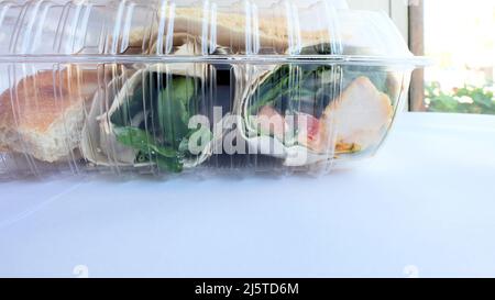 Klare Plastikreste-Behälter mit einem Huhn und Hummus-Wrap nach einer Mahlzeit im Restaurant übrig; verpackt oder verpackt zu Hause Lebensmittel zu nehmen. Stockfoto