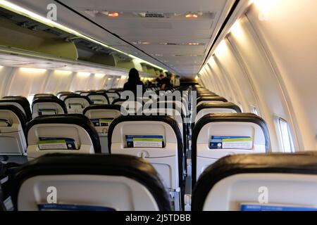 Die Innenkabine einer Boeing 737 von Alaska Airlines mit Rückenlehnen, Lichttafel und verschwommenen Passagieren in der Ferne zur Vorderseite des Flugzeugs. Stockfoto