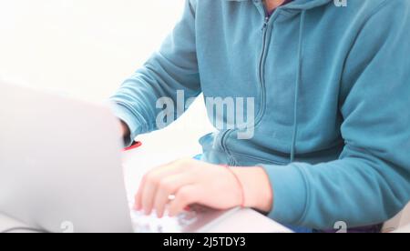 Ein Mann in einem türkisfarbenen Pullover in einem hellen Büro, während er an einem Computer in der Nähe arbeitet. Arbeitsdarstellung Stockfoto