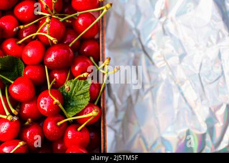 Unschärfe-Nahaufnahme-Box, Crape von dunkelroten, nassen Süßkirschen mit Schwanz und Blättern auf weißem Hintergrund. Sommerfrüchte und Beeren. Ernte und cr Stockfoto