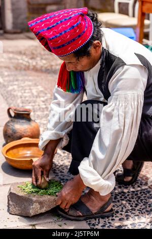 Ein Taquileno-Mann in traditioneller Tracht, Kräuter mahlen, Taquile Island, Titicacasee, Puno, Peru. Stockfoto