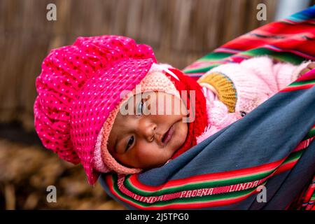 Ein Uros-Baby wird in Einem Sling auf den schwimmenden Uros-Inseln, dem Titicacasee, Puno, Peru, getragen. Stockfoto