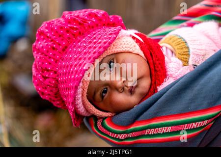 Ein Uros-Baby wird in Einem Sling auf den schwimmenden Uros-Inseln, dem Titicacasee, Puno, Peru, getragen. Stockfoto