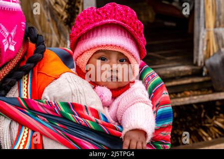 Ein Uros-Baby wird in Einem Sling auf den schwimmenden Uros-Inseln, dem Titicacasee, Puno, Peru, getragen. Stockfoto