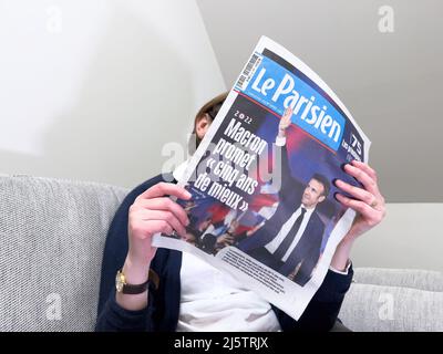 Paris, Frankreich - 25. Apr 2022: Frau liest auf einer gemütlichen Couch die neueste ZEITUNG LE Parisien berichtet über Frankreichs amtierender Präsident Emmanuel Macron, nachdem er Marine Le Pen für eine zweite fünfjährige Amtszeit geschlagen hatte Stockfoto