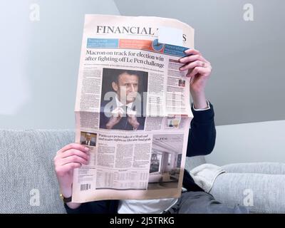 Paris, Frankreich - 25. Apr 2022: Frau liest auf einer gemütlichen Couch die neueste Zeitung der Financial Times berichtet über Frankreichs amtierenden Präsidenten Emmanuel Macron, nachdem sie Marine Le Pen für eine zweite fünfjährige Amtszeit geschlagen hatte Stockfoto