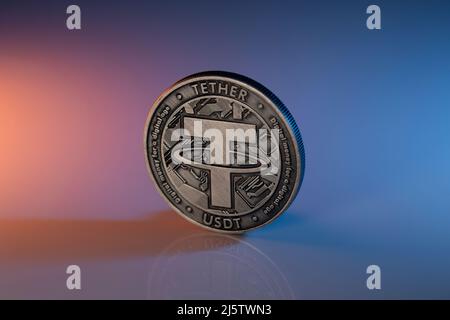 Tether USDT Cryptocurrency Physical Coin auf reflektierende Oberfläche platziert und mit orangefarbenen und blauen Lichtern beleuchtet. Stockfoto