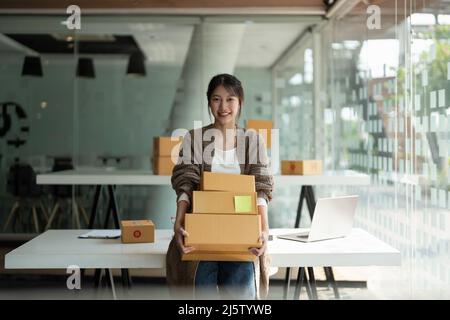 Kleinunternehmen gründen KMU-Inhaber weibliche Unternehmer, die Stapel von Boxen halten, um Bestellungen online zu überprüfen, um Boxen zu packen und an Kunden zu verkaufen Stockfoto