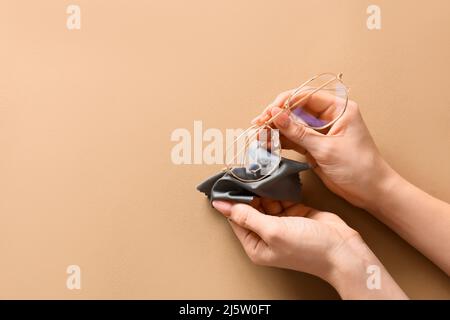 Weibliche Hände wischen Brillen auf beigem Hintergrund ab Stockfoto