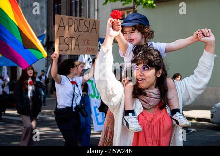 Porto, Portugal. 25. April 2022. Eine Frau trägt ein Kind, das eine Nelke hält. Die Parade vom 25.. April feiert die Nelkenrevolution, die 1974 stattfand. In Porto organisierten zivile Bewegungen eine Parade, die vor der inzwischen ausgestorbenen PIDE (politische Polizei) begann und direkt im Herzen der Stadt in der Avenida dos Aliados (Allies Avenue) endete. (Foto von Teresa Nunes/SOPA Images/Sipa USA) Quelle: SIPA USA/Alamy Live News Stockfoto