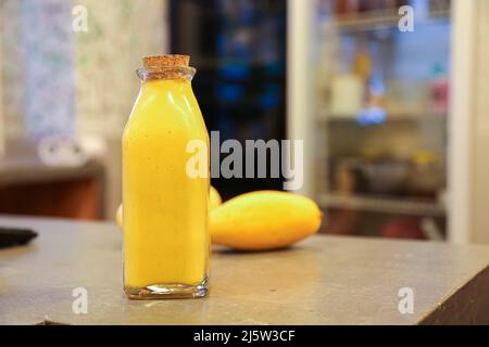 Mango Shake in Glasflasche mit Kork und frischen Mangos auf Küchenarbeitsplatte Stockfoto