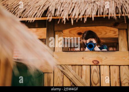 Junges Mädchen schaut durch das Teleskop auf den Zoo-Spielplatz Stockfoto