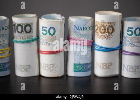 Auf dem Tisch stehen polnische Banknoten, die in einer Reihe zusammengerollt und mit einem Gummiband gebunden sind. Stockfoto