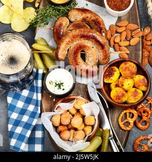 Oktoberfest Tischkonzept mit gegrillten Schweinswürsten, Brezelteig, Kartoffeln, Salat, Snacks, Saucen, Bier auf dunklem Hintergrund, Draufsicht. Stockfoto
