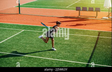 Powershot von einem Mädchen, das auf einem brandneuen Tennisplatz im Freien trainiert. Leuchtendes Grün und Braun mit klaren weißen Linien. Sich nach vorne lehnen und sie in sich stecken Stockfoto