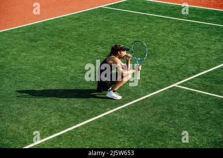 Hockte lachende Mädchen während des Trainings auf einem brandneuen Outdoor-Tennisplatz. Leuchtendes Grün und Braun mit klaren weißen Linien. Stockfoto