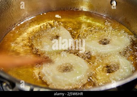 Kochen von Apfelpfannkuchen. Der Küchenchef dreht den Apfeldonut in das kochenden Öl Stockfoto