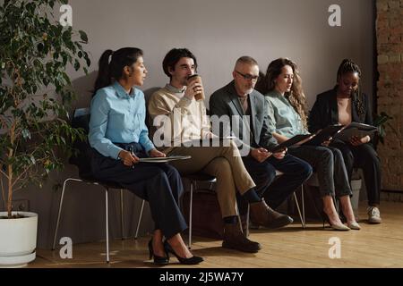 Gruppe von Menschen, die auf Stühlen im Wartezimmer mit Lebensläufen sitzen und auf ihr Vorstellungsgespräch warten Stockfoto