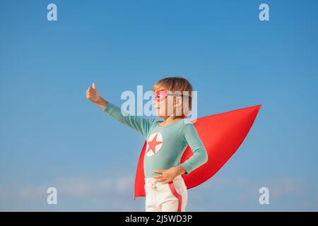 Superheld Kind spielt draußen. Super Held Kind vor blauem Sommerhimmel Hintergrund. Vorstellung und Freiheit Konzept Stockfoto